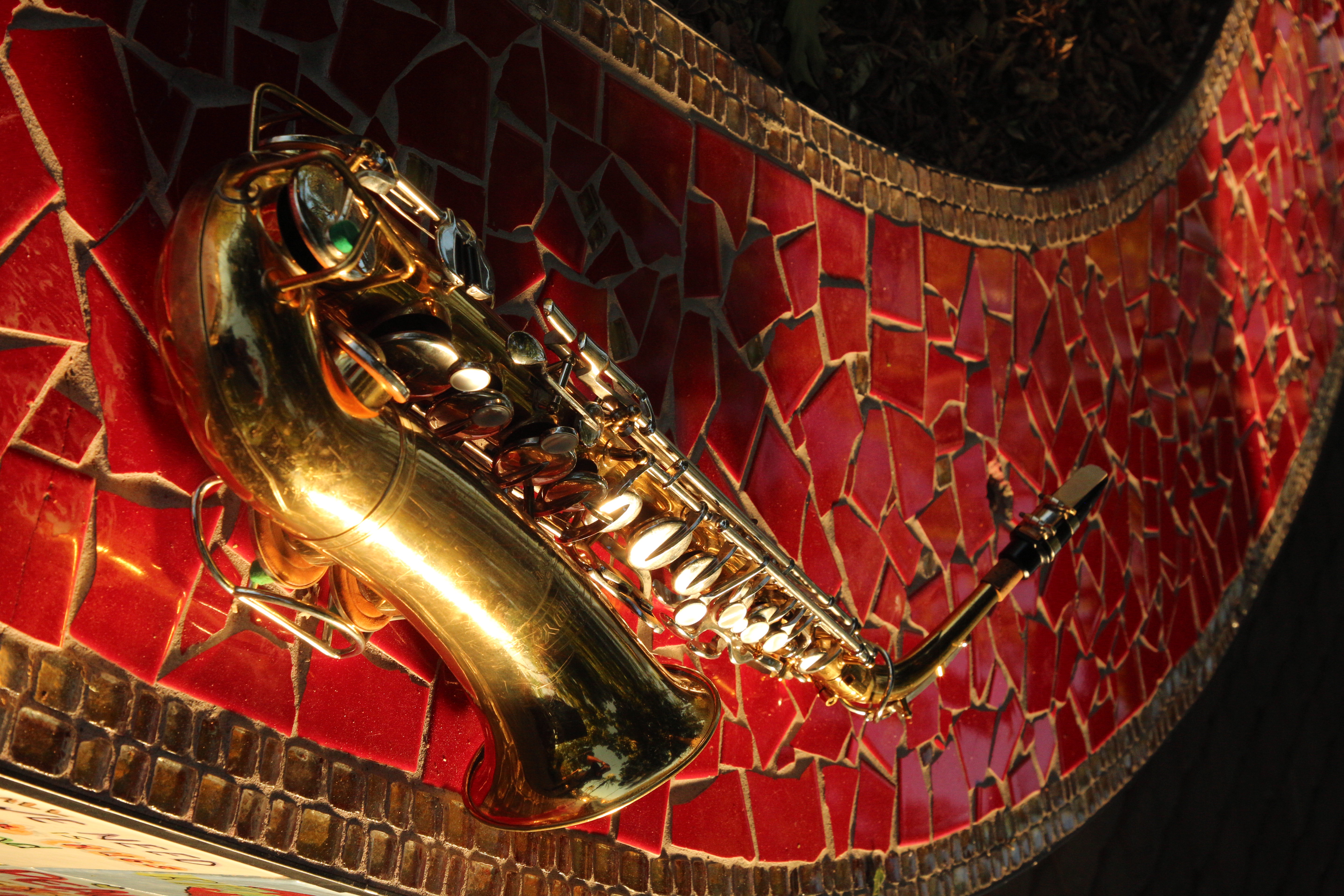 Golden saxophone resting on a red mosaic-tile bench in warm golden-hour light